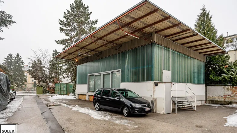 Modernes Gebäude mit Glasfassade und Holzdach, umgeben von Schnee und Bäumen, mit einem geparkten Auto davor.