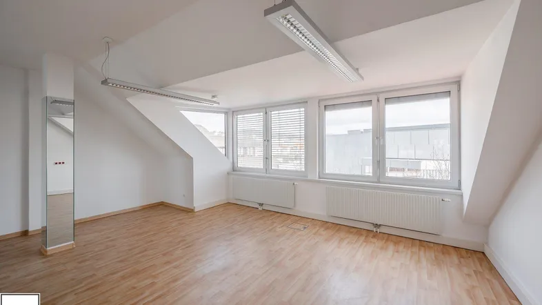 Geräumiger, heller Büroraum im Dachgeschoss mit großen Fenstern und Holzfußboden.