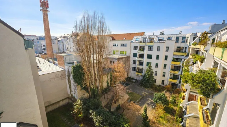 Blick auf einen begrünten Innenhof mit umliegenden Gebäuden und einem markanten Schornstein im Hintergrund.