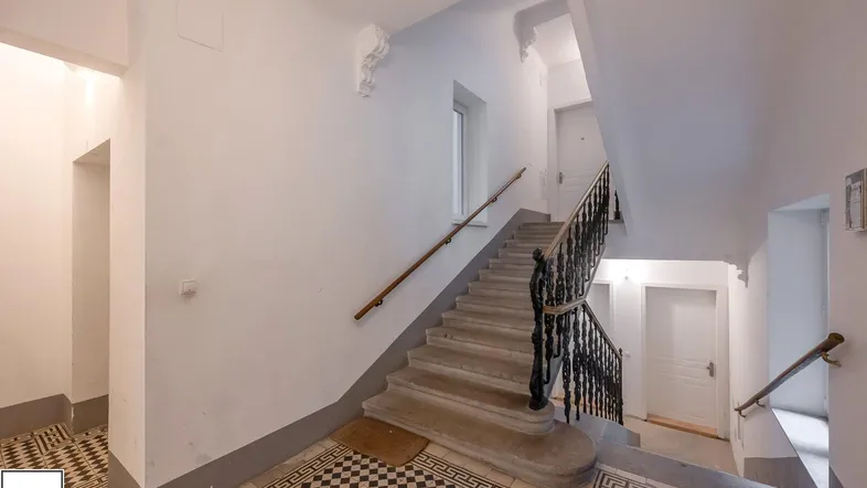 Helles Treppenhaus mit kunstvollen Fliesenböden, hohen Decken und schmiedeeisernem Geländer.