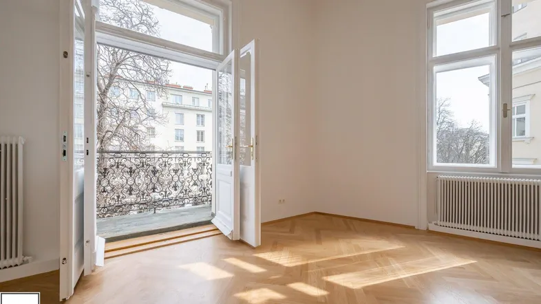 Helles Zimmer mit Zugang zu einem französischen Balkon und Fischgrätparkettboden.
