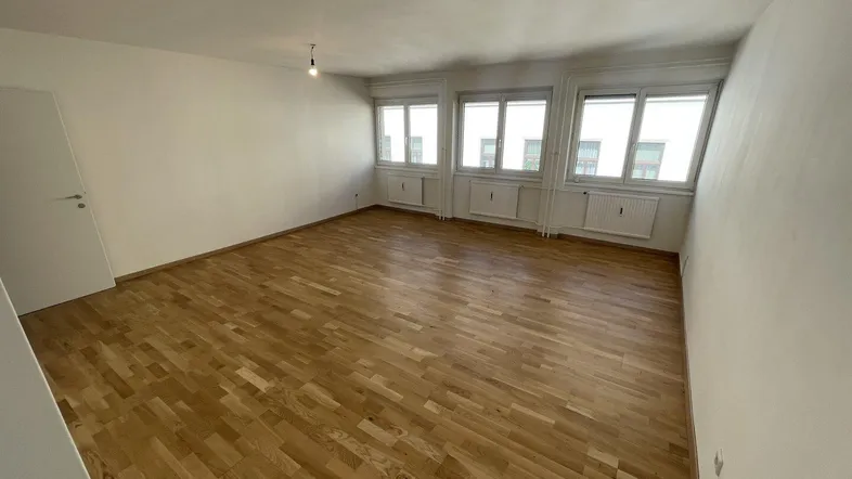 Heller, leerer Raum mit Parkettboden und mehreren Fenstern, ideal als Wohn- oder Schlafzimmer.