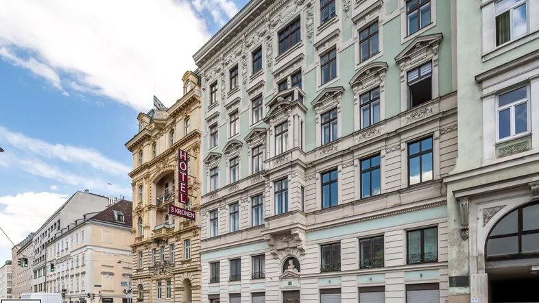 Historisches Gebäude mit klassischer Fassade und Geschäften im Erdgeschoss an einer belebten Straße.