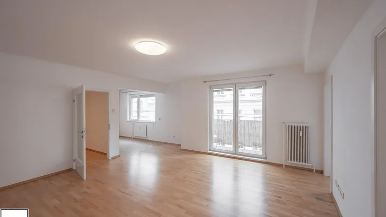 Helles Wohnzimmer mit Parkettboden, weißen Wänden und Zugang zu einem Balkon.