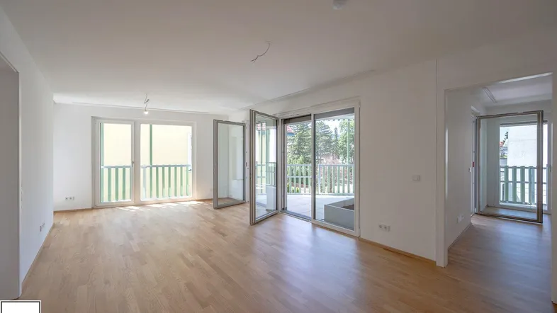 Helles, leeres Wohnzimmer mit Parkettboden und Zugang zu mehreren Balkonen, ideal für individuelle Gestaltung.
