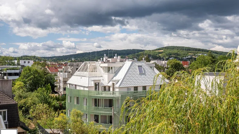 Blick auf ein modernes Gebäude mit grüner Fassade und umliegender Hügellandschaft unter bewölktem Himmel.