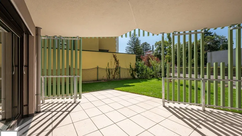 Große geflieste Terrasse mit Zugang zum Garten und grünen Sichtschutzelementen.