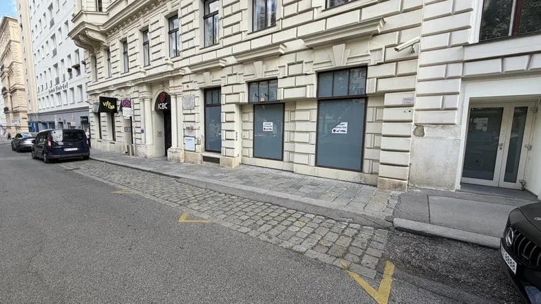 Blick auf die historische Fassade eines Gebäudes mit Geschäften im Erdgeschoss und geparkten Autos.
