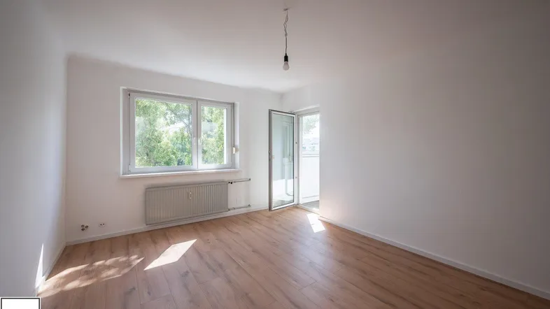 Helles Zimmer mit neuem Laminatboden, weißen Wänden und Zugang zu einem Balkon.