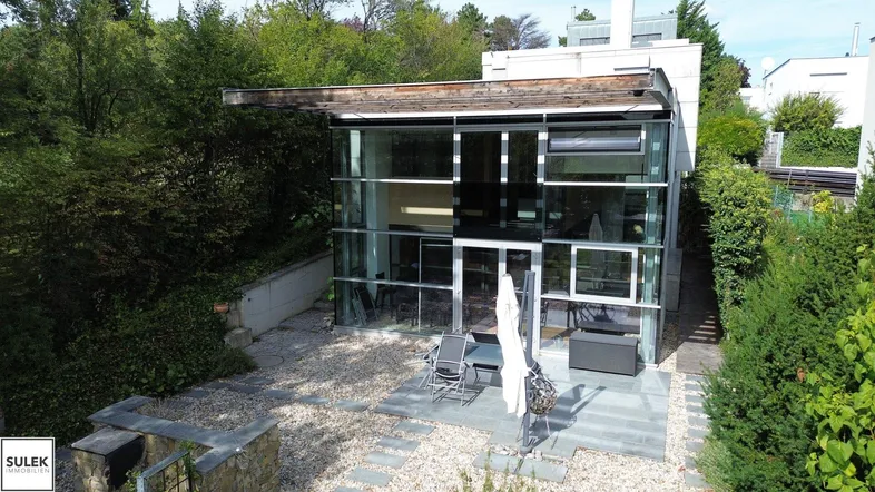 Moderne Glasfassade eines Hauses mit Kiesgarten und möblierter Terrasse unter freiem Himmel.