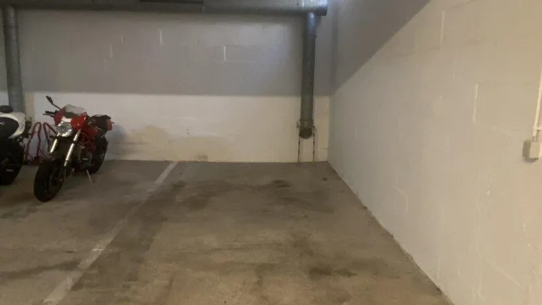 Geräumiger Tiefgaragenstellplatz mit Betonboden und sichtbaren Leitungen, beleuchtet durch kleine Fenster.