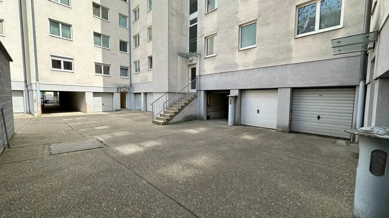 Außenansicht eines Mehrfamilienhauses mit mehreren Garagen und einem gepflasterten Vorplatz.
