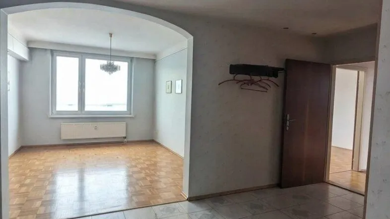 Geräumiger Wohnbereich mit Fliesenboden und Parkett in angrenzendem Zimmer, hell durch großes Fenster.