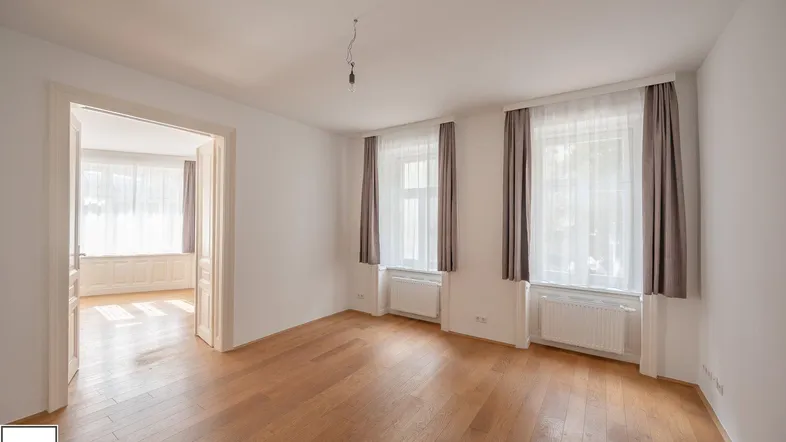 Helles Zimmer mit Holzparkettboden und zwei Fenstern, das viel Tageslicht hereinlässt.