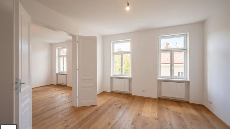 Helles, leeres Zimmer mit neu verlegtem Holzboden und großen Fenstern, bereit zur Gestaltung.