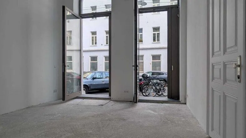 Heller, leerer Raum mit hohen Decken und zwei großen Rundbogenfenstern zur Straße hin.