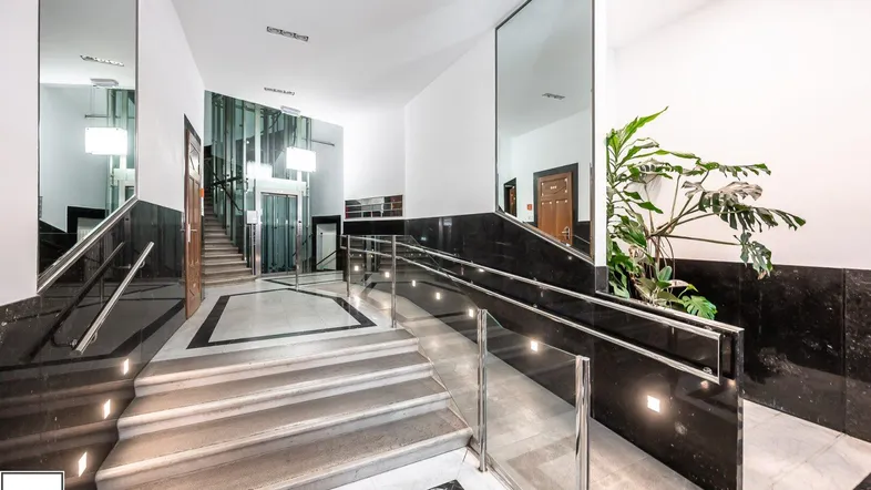Helle Eingangshalle mit Treppe, Rampe und modernem Glasaufzug, ausgestattet mit dunklem Marmor.