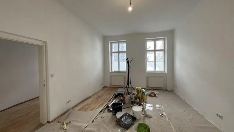 Heller Raum in Renovierung mit weißen Wänden und teilweise freigelegtem Holzfußboden, bereit zur Neugestaltung.