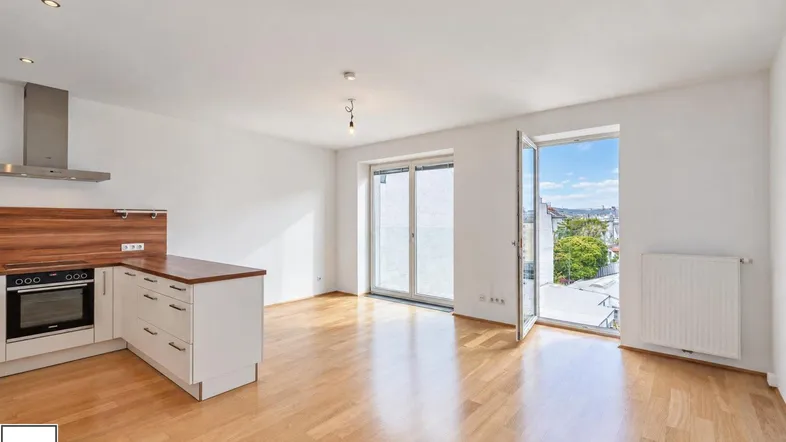 Heller offener Wohnbereich mit integrierter Küche, Parkettboden und Zugang zu einem Balkon mit Stadtblick.