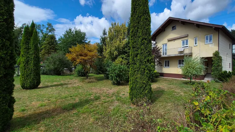 Großzügiger Gartenbereich mit hohen Bäumen und Blick auf das Wohnhaus unter blauem Himmel.