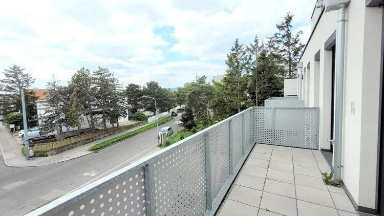 Geräumiger Balkon mit Fliesenboden und Blick auf die Straße sowie umliegende Bäume.