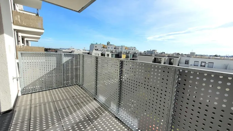 Heller Balkon mit perforiertem Metallgeländer und Blick auf die umliegenden Gebäude.