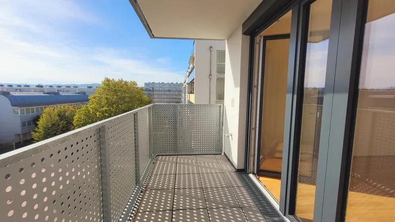 Geräumiger Balkon mit perforiertem Metallgeländer und Blick auf die Umgebung.
