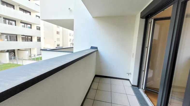 Heller Balkon mit Fliesenboden und Blick auf die umliegenden Wohngebäude in einer modernen Anlage.