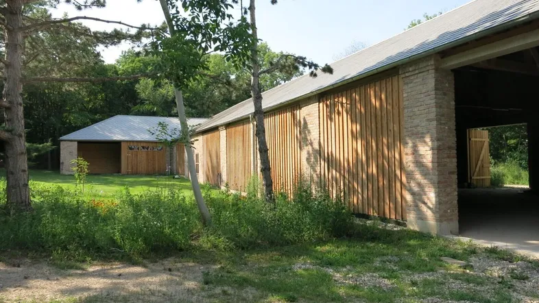Langes Gebäude mit Holzverkleidung und Ziegelmauerwerk, umgeben von viel Grün und Bäumen.