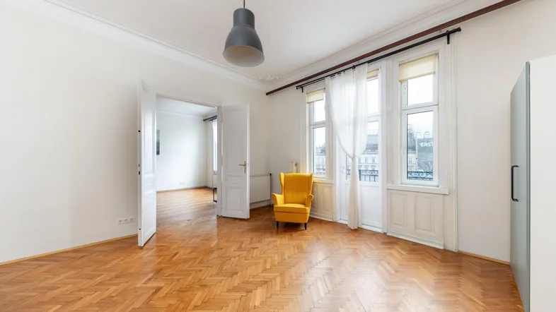 Helles Wohnzimmer mit Fischgrätparkett, hohen Decken und Stuckverzierungen, durch große Fenster lichtdurchflutet.