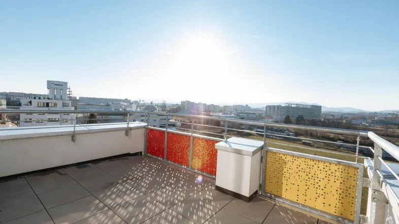 Sonnige Dachterrasse mit urbanem Ausblick und farbigen Brüstungselementen.