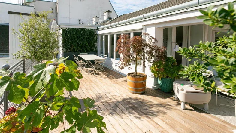 Geräumige Dachterrasse mit Holzdeck, Esstisch und üppiger Bepflanzung für entspannte Stunden im Freien.
