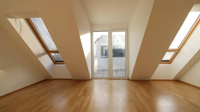 Geräumiges, leeres Wohnzimmer mit Parkettboden, Dachschrägen und Zugang zu einem Balkon.