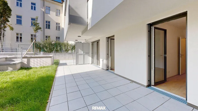 Große geflieste Terrasse mit angrenzender Rasenfläche und Zugang zum Innenbereich.