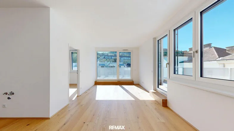 Helles, leeres Zimmer mit Holzboden und großen Fenstern, die Zugang zu einem Balkon bieten.