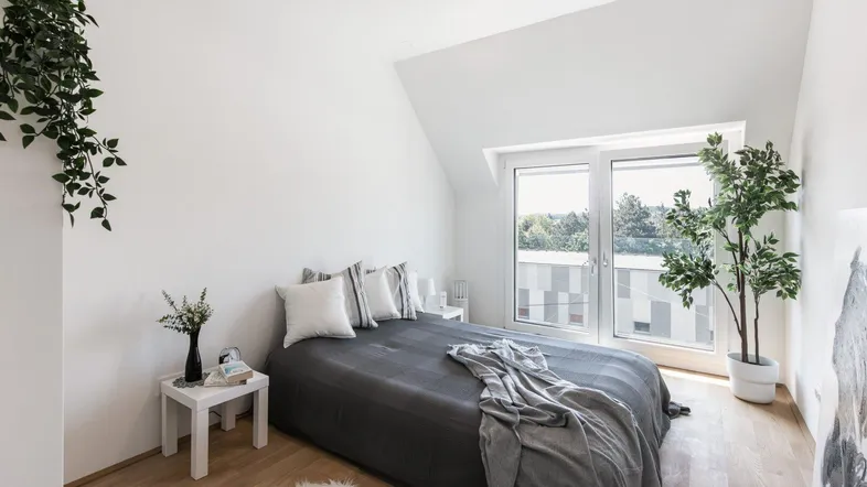 Helles Schlafzimmer mit Holzboden, Zugang zum Balkon und schräger Decke im Dachgeschoss.