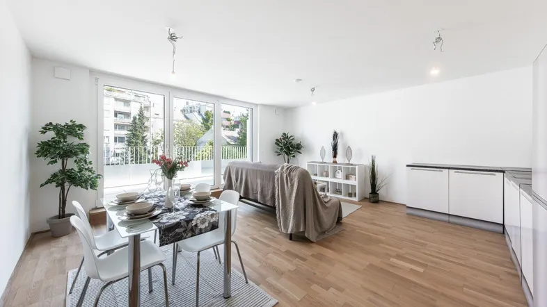 Heller, offener Wohn- und Essbereich mit integrierter Küche, großen Fenstern und Holzboden.