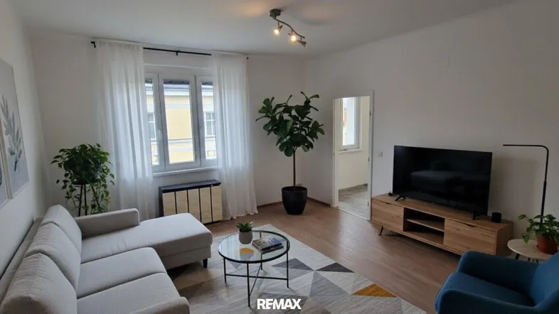 Helles Wohnzimmer mit beigem Sofa, Holzboden und Blick auf die Straße.