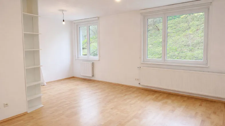 Helles Zimmer mit Parkettboden, weißen Wänden und Blick ins Grüne, ausgestattet mit Einbauregalen.
