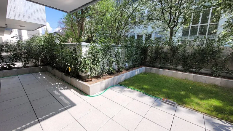 Gepflasterte Terrasse mit kleinem Rasenbereich und grünen Hecken, ideal für Entspannung im Freien.