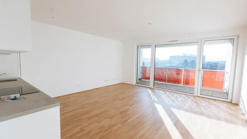 Heller, offener Wohnbereich mit Holzboden und großem Fenster zum sonnigen Balkon.