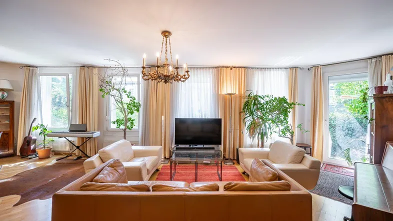 Helles Wohnzimmer mit bequemen Sofas, Kronleuchter und großen Fenstern mit Blick ins Grüne.