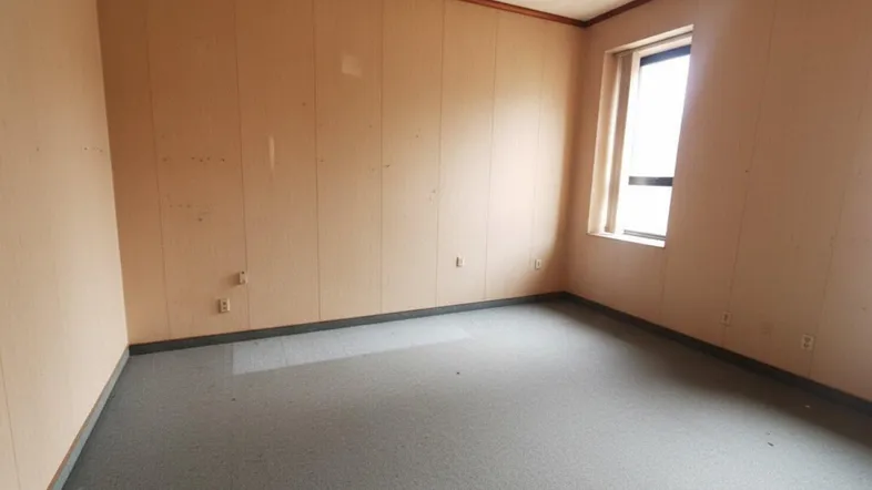 Leerer Raum mit Teppichboden, Holzvertäfelung und einem Fenster, ideal als Arbeitszimmer.