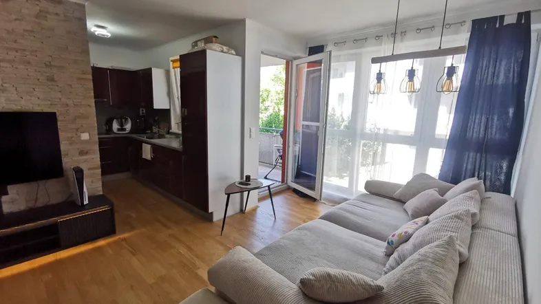 Heller offener Wohn- und Essbereich mit Holzboden, beigem Sofa und Zugang zum Balkon.