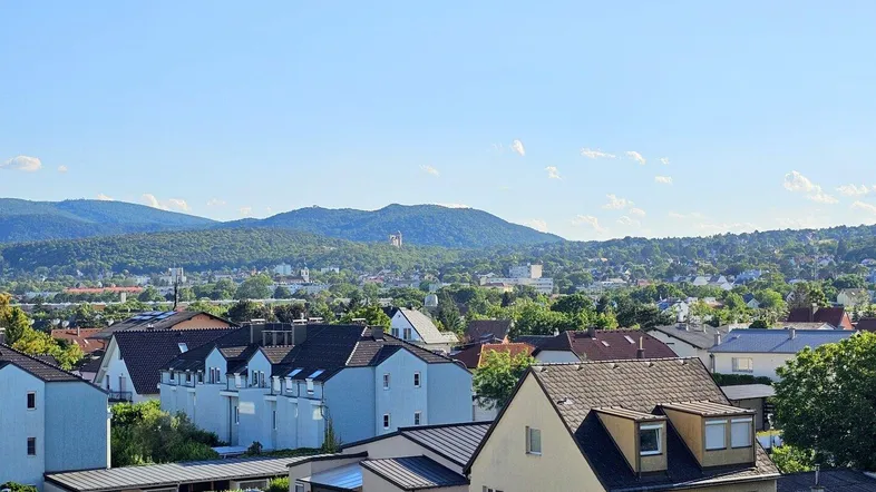 Blick über die Dächer der Stadt auf die umliegende grüne Landschaft und Berge.
