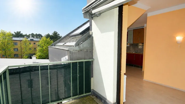 Sonniger Balkon mit Blick ins Grüne und Zugang zu einem hellen Innenraum.
