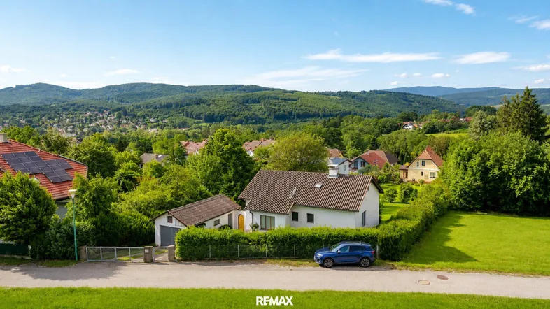 Weitläufige Luftaufnahme des Hauses mit umliegender grüner Landschaft und Bergen im Hintergrund.