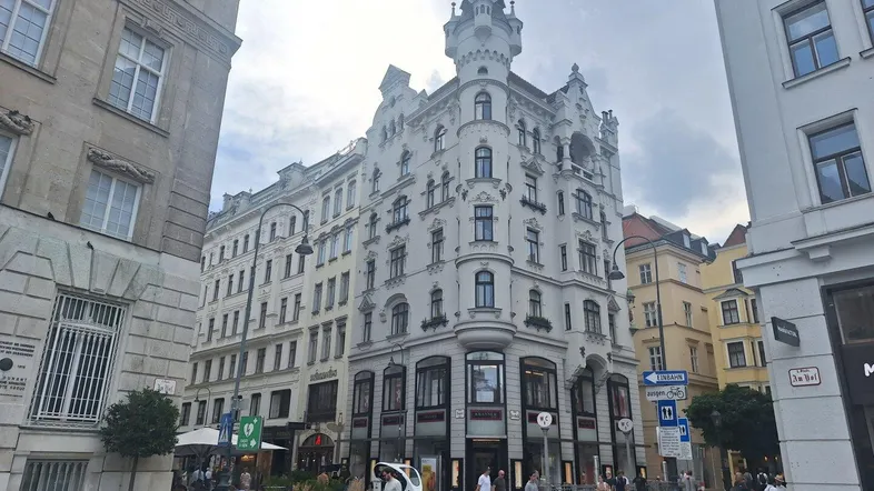 Historisches Gebäude mit markanter Architektur und Turm in einer belebten Stadtstraße.