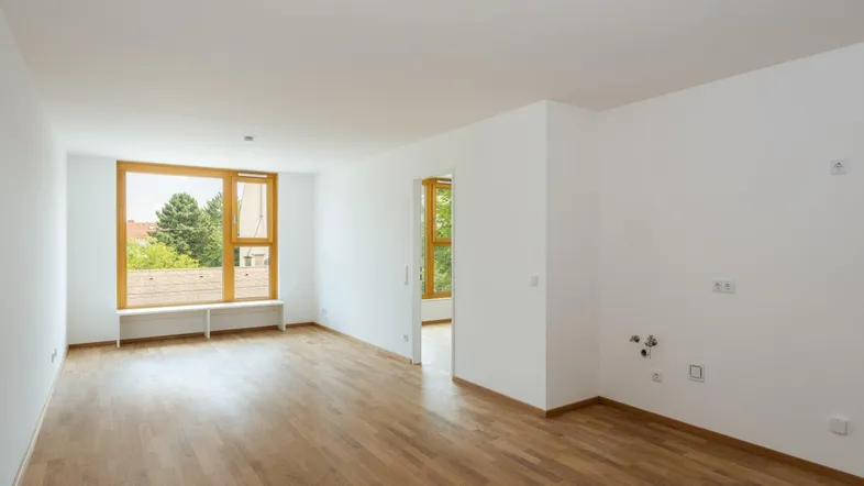 Helles Zimmer mit Holzboden und großen Fenstern, die einen grünen Ausblick bieten.