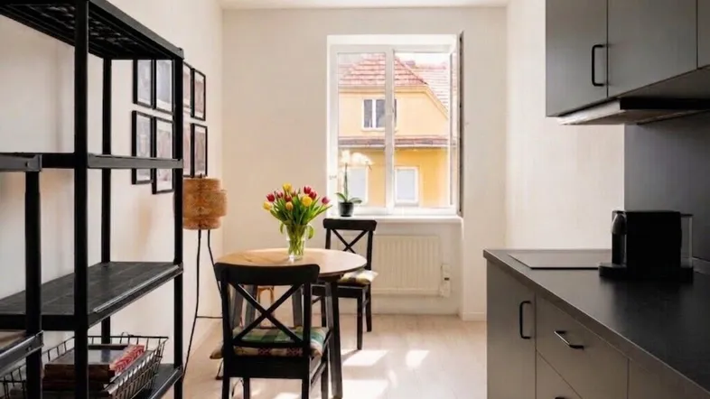 Moderne Küchenzeile mit schwarzen Schränken und Essbereich, hell durch ein Fenster mit Blick auf ein Nachbargebäude.